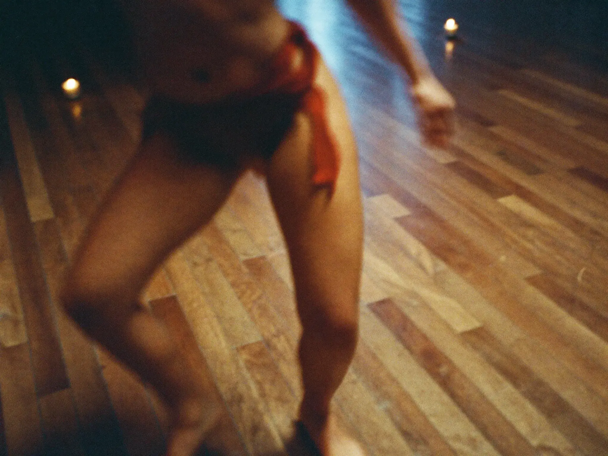 Close-up of a bachata dancer’s legs and hips mid weight-transfer on a warm candlelit floor